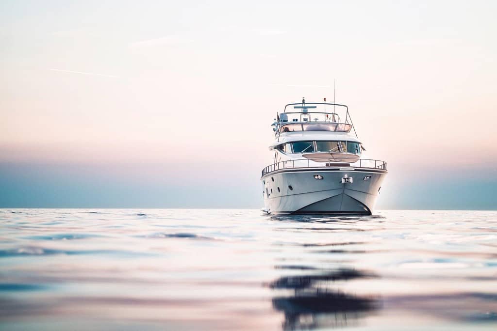 A luxury yacht afloat in the calm waters of Los Cabos at dusk, with soft pastel skies in the background.