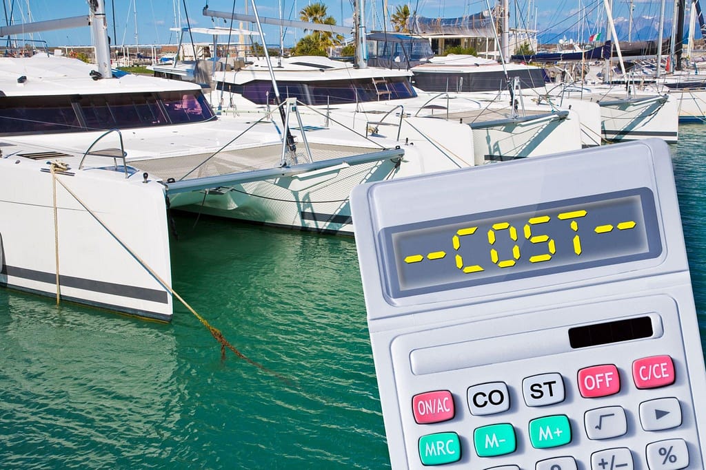 A calculator with the word "-COST-" on its display in the foreground, with luxury yachts docked in a marina, possibly in Los Cabos, in the background.