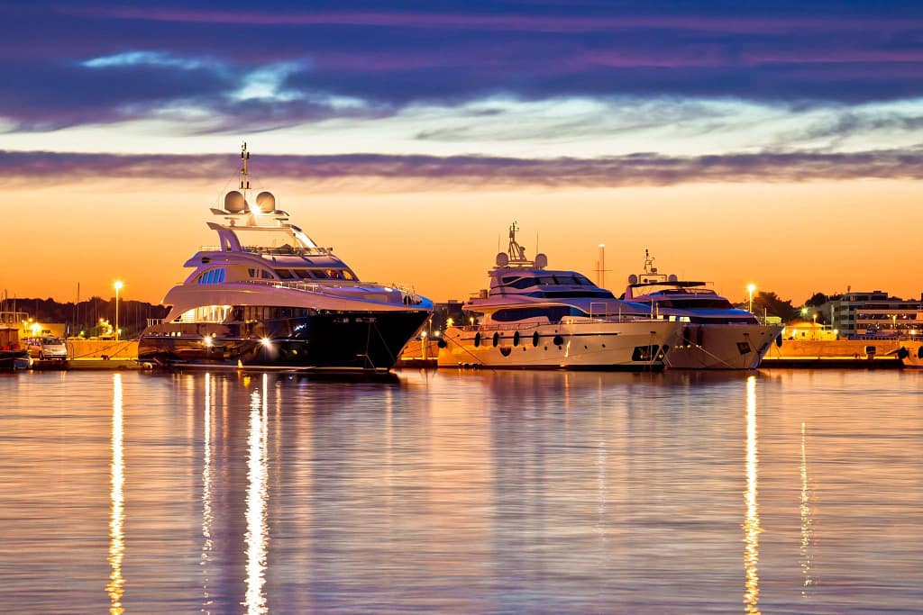 Luxury yachts moored in a harbor at sunset, with a warm sky reflecting off the calm waters, possibly in Los Cabos.
